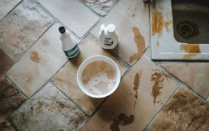 Natural stone tile floor with cleaning products and water stains near a kitchen sink.